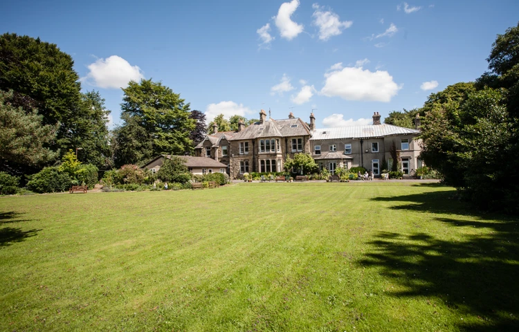 A huge garden with large trees and Cove House in the distance