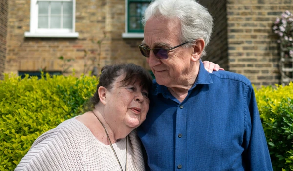 Older Woman Resting Head On Older Man's Shoulder In Street