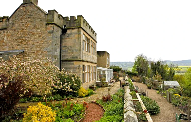 A grand stone building with turrets and beautiful gardens