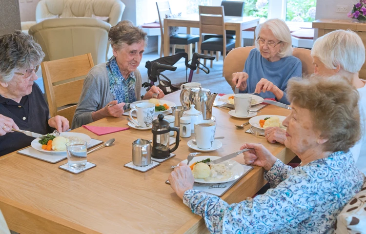 Five residents are sat around a table enjoying dinner