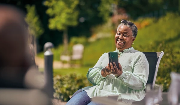 Older Woman Sitting On Bench In Garden Whilst Chatting On Phone
